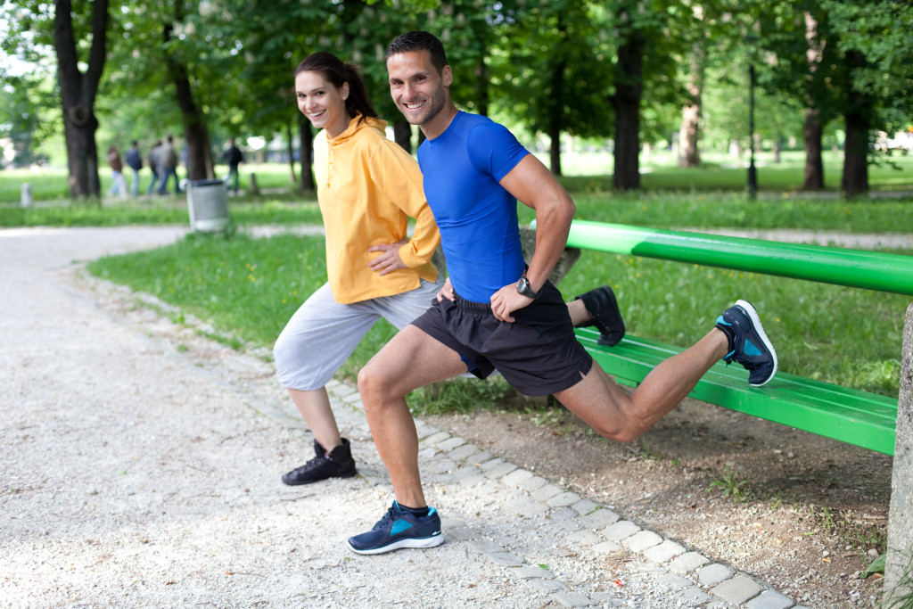 Happy young couple exercising outdoors, using a park bench to do